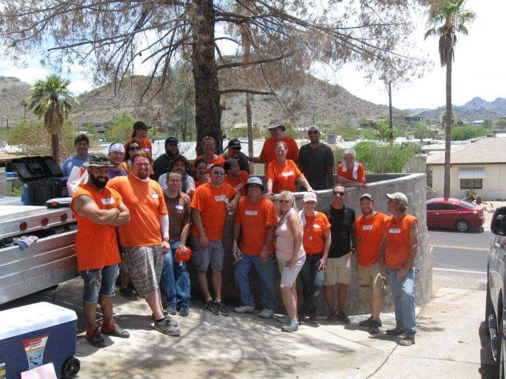 A group of people in orange shirts posing outdoors near trees and buildings.